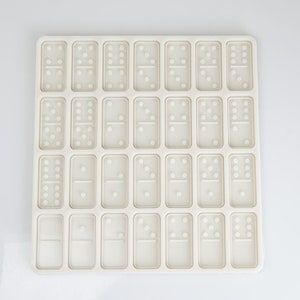May include: A white silicone mold with 28 individual domino-shaped cavities. The mold is designed for making chocolate or candy dominoes.