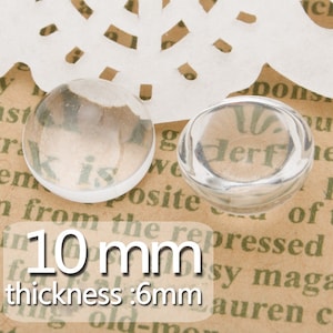 May include: Two clear glass cabochons, one 10 mm in diameter and the other 6 mm thick, on a brown surface with text.
