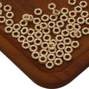 May include: A large quantity of gold-colored metal jump rings. The rings are arranged in a pile on a wooden surface.