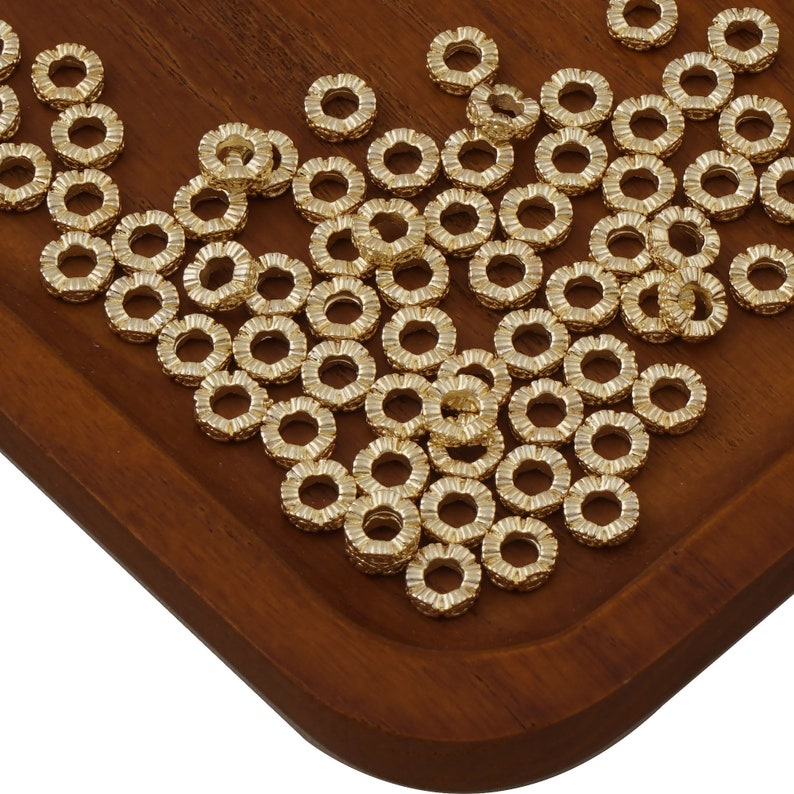 May include: A large quantity of gold-colored metal jump rings. The rings are arranged in a pile on a wooden surface.