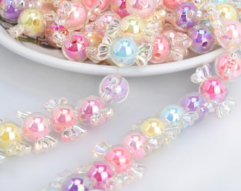 May include: A pile of iridescent candy-shaped beads in various pastel colors, including pink, blue, yellow, and purple. The beads are strung together in a necklace.
