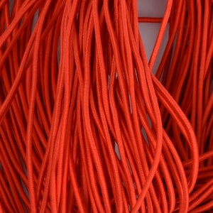 May include: A close-up of a bundle of bright orange elastic cord. The cord is smooth and appears to be made of a stretchy material.