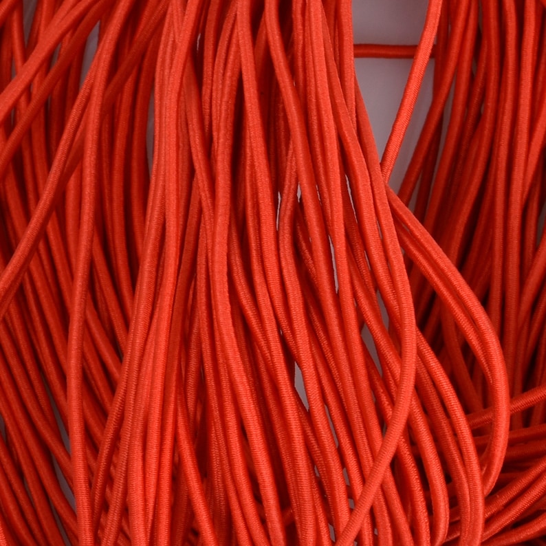 May include: A close-up of a bundle of bright orange elastic cord. The cord is smooth and appears to be made of a stretchy material.