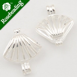 May include: Two silver-toned metal shell-shaped bead caps with a fan-like design. The caps are open on one side and have a loop on the top for attaching to a necklace or bracelet.