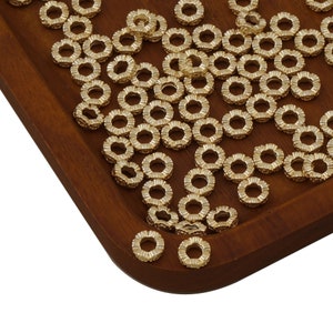 May include: A large quantity of gold-colored metal spacer beads. The beads are round with a decorative, scalloped edge. The beads are arranged on a wooden surface.