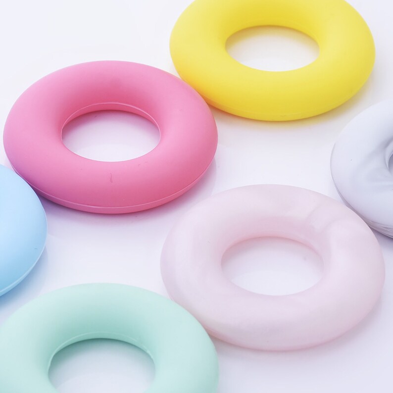 May include: Six colorful silicone rings in various colors, including pink, yellow, light blue, light green, and white. The rings are shaped like a donut and are arranged in a semi-circle on a white background.