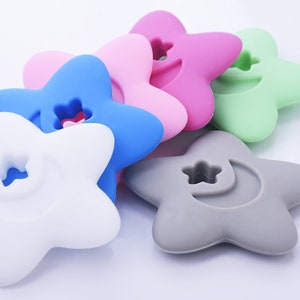 May include: Six silicone star-shaped teethers in various colors, including blue, pink, white, gray, and green. Each teether has a small hole in the center and a crescent moon shape on one side.