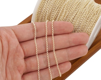 May include: A spool of gold-colored chain, with three strands of the chain laid out on a hand. The chain is a delicate, fine-link style.