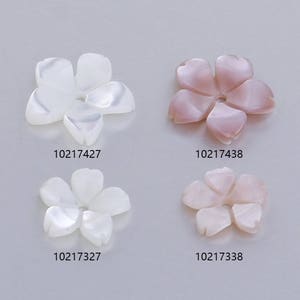 May include: Four flower-shaped shell beads, two white and two pink. The beads are arranged in a grid pattern. The beads are approximately 1 inch in diameter.