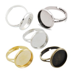 May include: Five adjustable ring blanks with round glass cabochon settings. The rings are made of silver, gold, and bronze metal. The glass cabochons are clear, gold, and black.