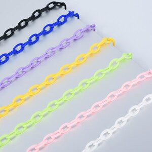 May include: Seven plastic chains in different colours: black, blue, purple, yellow, green, pink, and white. The chains are laid out in a row on a light grey surface.