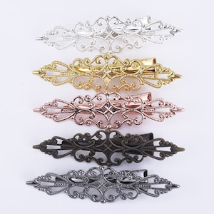 Könnte beinhalten: Fünf verzierte Haarklammern in verschiedenen Metallic-Farben: Silber, Gold, Roségold, Bronze und Gunmetal. Jede Klammer hat ein zartes, filigranes Design.