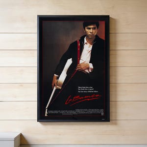 May include: A framed movie poster for La Bamba featuring a man in a black jacket and white shirt holding a white guitar with a red strap. The text reads Talent Made him a Star. Fate Made him a Legend. The True Story of Ritchie Valens.