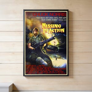 May include: A framed movie poster for "Missing in Action" featuring Chuck Norris. The poster has a dark color scheme with a jungle scene, a helicopter, and the film's title in large, bold letters. The text "The war's not over until the last man comes home!" is also visible.