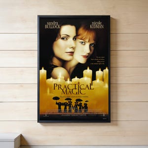 Może przedstawiać: Oprawiony plakat filmowy do filmu "Practical Magic" z Sandrą Bullock i Nicole Kidman. Plakat ma czarną ramę i przedstawia twarze aktorek nad tytułem, z zapalonymi świecami i sylwetkami osób z parasolami.