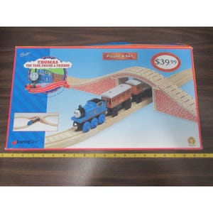 May include: A boxed Thomas the Tank Engine wooden train set. The set includes a blue Thomas engine, two brown passenger cars, and a wooden track with a brick bridge. The box reads "Figure 8 Set".
