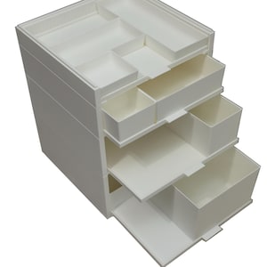 Puede incluir: Un organizador de almacenamiento de plástico blanco con múltiples cajones y compartimentos. La sección superior presenta una variedad de pequeñas bandejas abiertas. Varios cajones están parcialmente extraídos, revelando el espacio de almacenamiento interior.