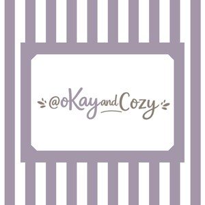 May include: A white background with a lavender frame and vertical stripes. The text "@Kay and Cozy" is written in a script font within the frame. The text is in shades of lavender and brown.