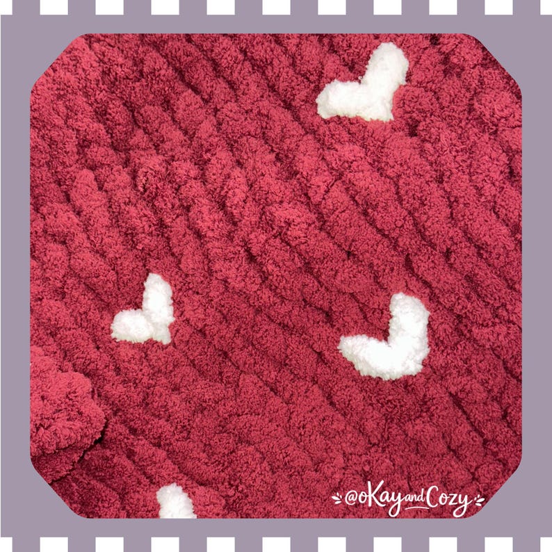 May include: A burgundy chunky knit blanket with white heart-shaped accents. The blanket has a soft, textured appearance and is suitable for home decor. The text "@Kay and Cozy" is in the bottom right corner.