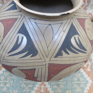 May include: A brown ceramic pot with a geometric design in black and red. The pot has a wide mouth and a rounded body.