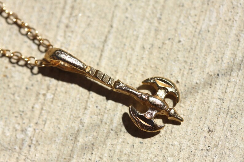 May include: A gold-toned necklace with a pendant shaped like a double-headed axe.