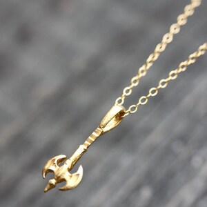 May include: A gold necklace with a small axe pendant. The axe is detailed with a textured handle and a double-bladed head.