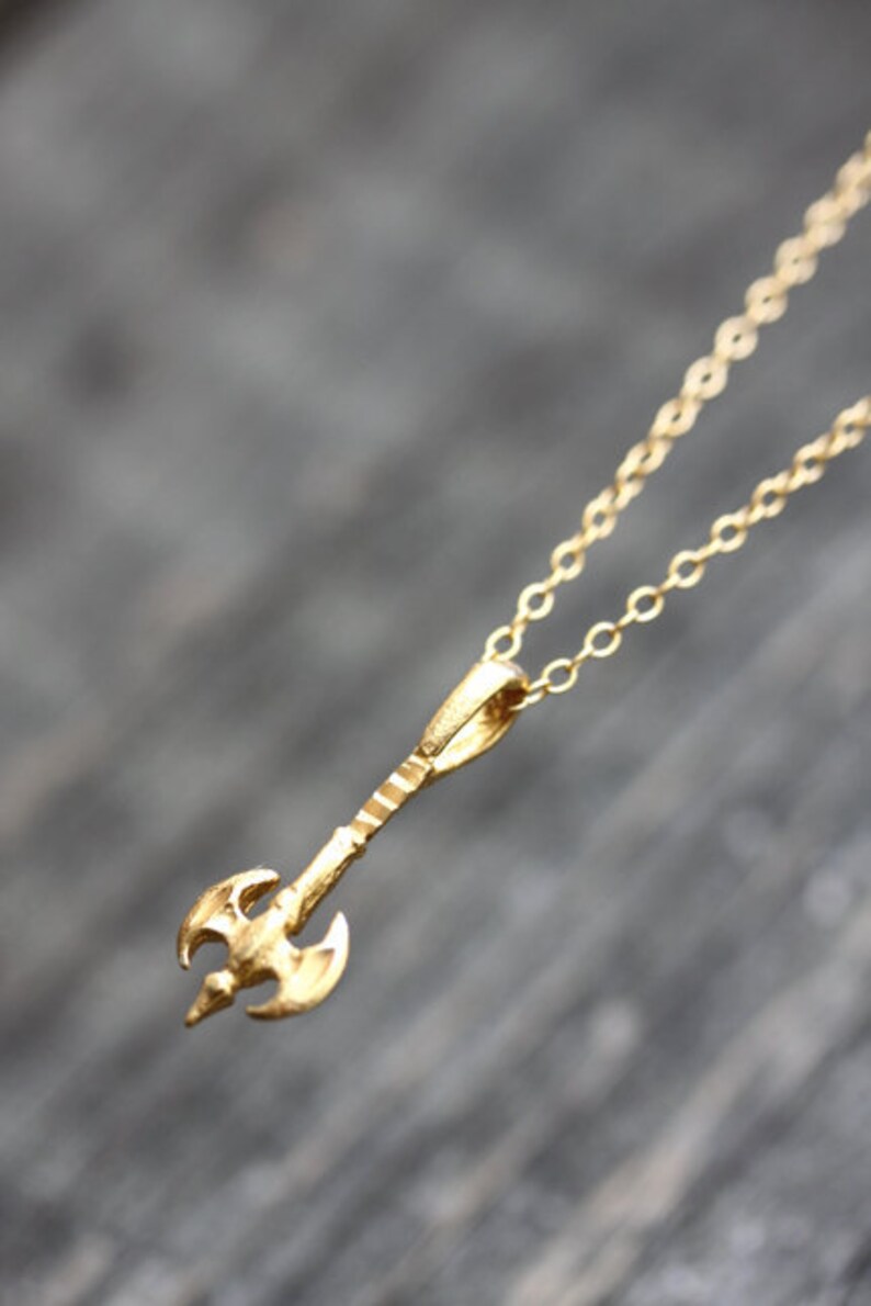 May include: A gold necklace with a small axe pendant. The axe is detailed with a textured handle and a double-bladed head.