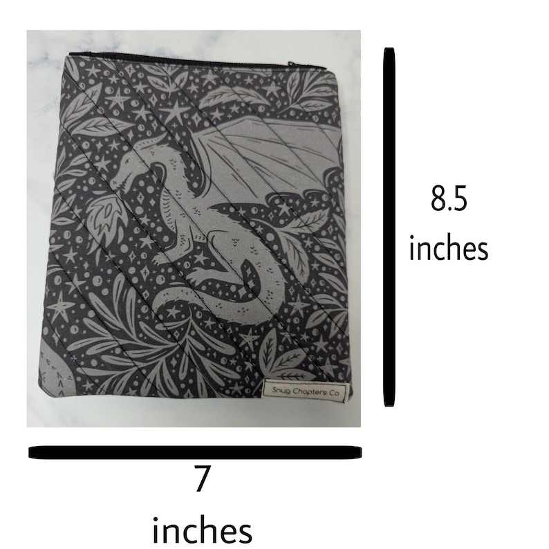 Op de afbeelding: Een donkergrijs tasje met rits voorzien van een lichtgrijs patroon van een draak, sterren en bladeren. Het tasje heeft diagonale doorgestikte naden en een klein label met Snug Chapters Co. Het is 21,59 cm hoog en 17,78 cm breed.