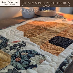 May include: Close-up of a quilted fabric with floral and geometric patterns. The quilt features a mix of colors, including cream, brown, and navy blue. The text "Honey & Bloom Collection" and "Wild Garden Honey" are visible.