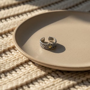 May include: An open-band ring featuring a silver-toned finish with a textured, dark-oxidized surface pattern. The center of the ring displays a small, circular gold-toned sun motif with radiating lines, creating a distinct contrast against the silver.