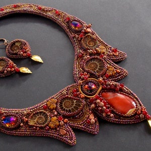 May include: A beaded necklace and earrings set with a large red agate stone, brown ammonite fossils, and gold accents. The necklace is a statement piece with a unique design.