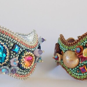 May include: Two beaded bracelets with a wavy design. One bracelet is silver with blue, green, and pink beads. The other bracelet is brown with green, pink, and gold beads.