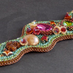 May include: A beaded bracelet with a wavy design, featuring a variety of colourful beads, including turquoise, pink, green, and brown. The bracelet has a metal clasp.
