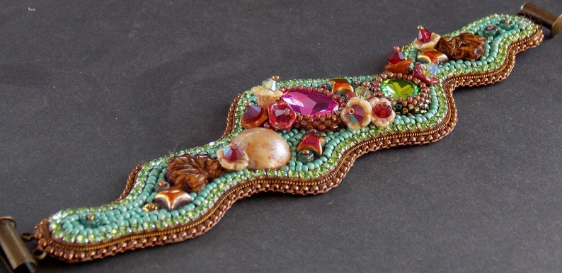 May include: A beaded bracelet with a wavy design, featuring a variety of colourful beads, including turquoise, pink, green, and brown. The bracelet has a metal clasp.