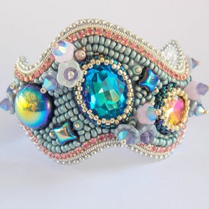 May include: A beaded bracelet with a wavy design, featuring a large blue gemstone, iridescent beads, and pink and purple accents.