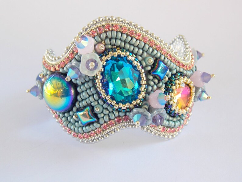 May include: A beaded bracelet with a wavy design, featuring a large blue gemstone, iridescent beads, and pink and purple accents.