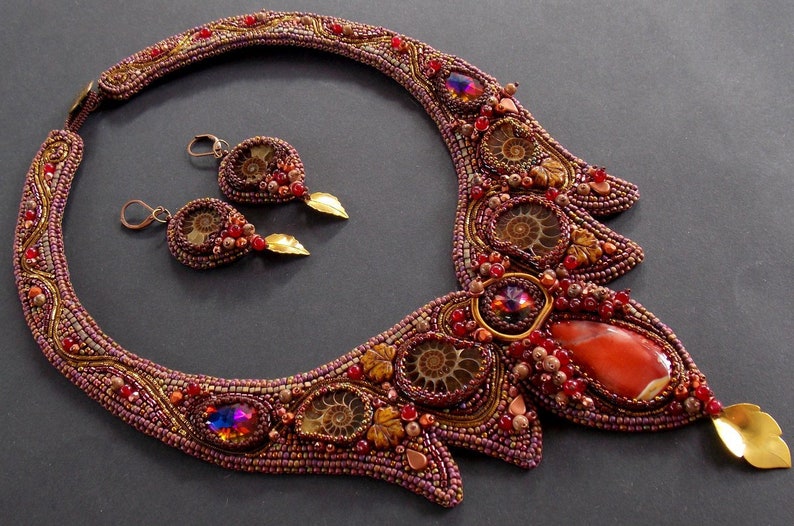 May include: A beaded necklace and earrings set with a large red agate stone, brown ammonite fossils, and gold accents. The necklace is a statement piece with a unique design.