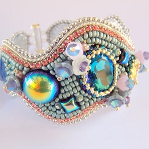 May include: A beaded bracelet with a wavy design, featuring a variety of colourful beads, including iridescent, blue, pink, and gold. The bracelet is adorned with a large, faceted, teal gemstone.