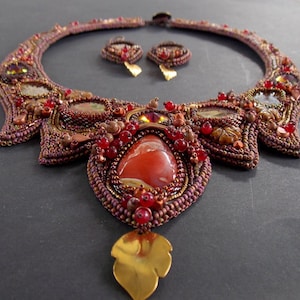 May include: A beaded necklace with a large red agate stone pendant and matching earrings. The necklace is made with brown, gold, and red beads and features a leaf-shaped pendant.