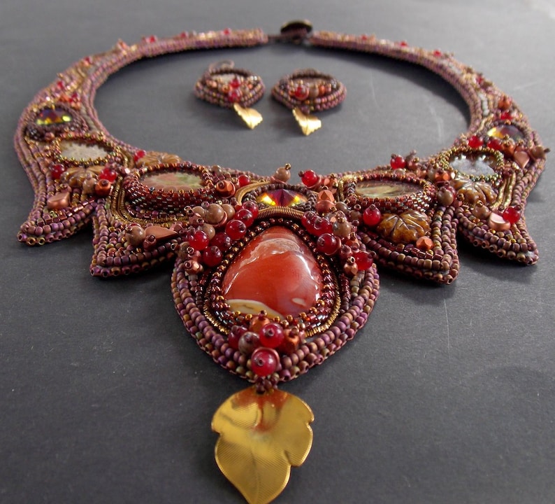 May include: A beaded necklace with a large red agate stone pendant and matching earrings. The necklace is made with brown, gold, and red beads and features a leaf-shaped pendant.