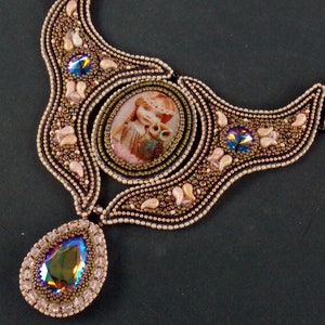 May include: A beaded necklace with a large, oval-shaped pendant featuring a girl and an owl. The pendant is surrounded by smaller beads and crystals. The necklace is made of brown, gold, and pink beads.