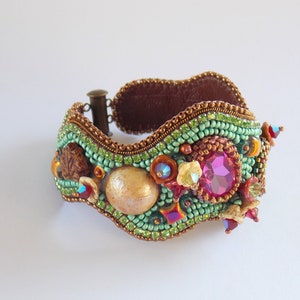 May include: A beaded bracelet with a wavy design, featuring a large pink gemstone, a shell, and other colourful beads.