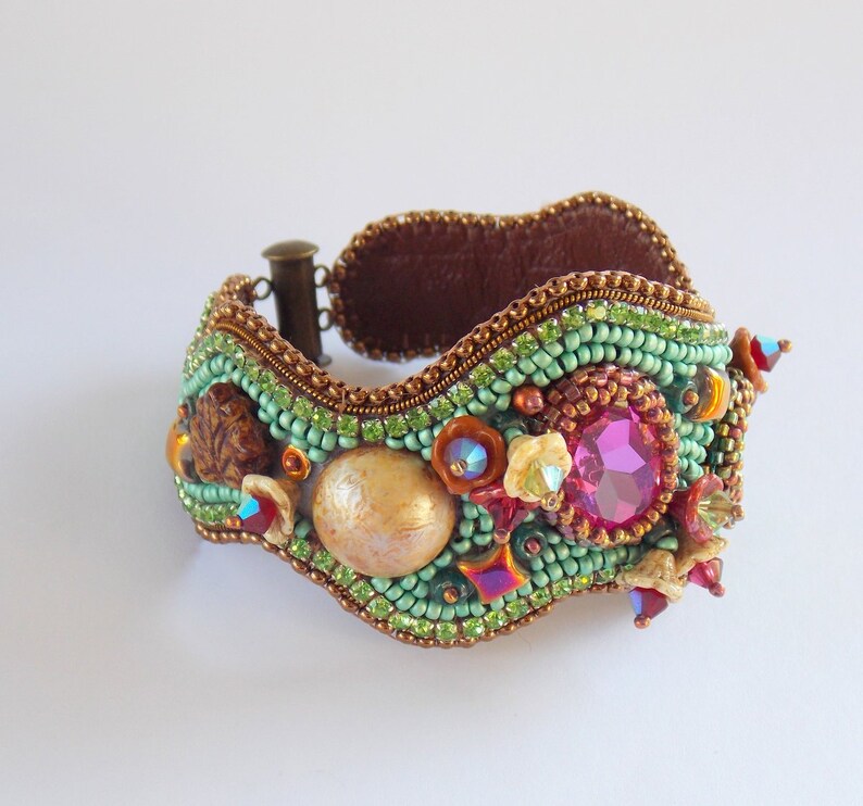 May include: A beaded bracelet with a wavy design, featuring a large pink gemstone, a shell, and other colourful beads.