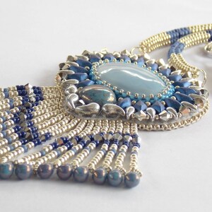 Puede incluir: Un collar de cuentas plateadas y azules con un gran colgante de piedra preciosa azul y una franja de cuentas.