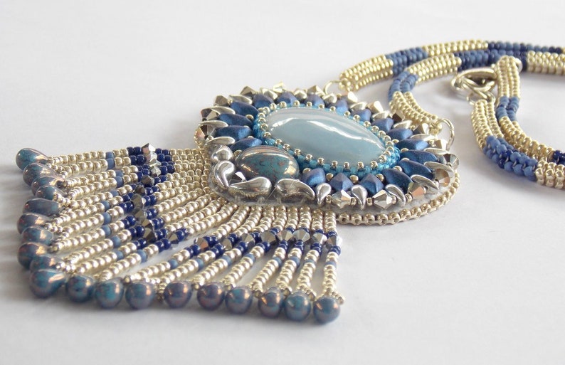 Puede incluir: Un collar de cuentas plateadas y azules con un gran colgante de piedra preciosa azul y una franja de cuentas.