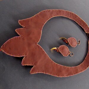 May include: A brown leather necklace with a gold pendant and matching earrings. The necklace is decorated with small beads and the earrings have a teardrop shape.