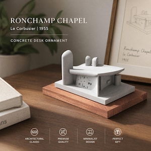 May include: Concrete desk ornament of the Ronchamp Chapel, designed by Le Corbusier in 1955. The model is light gray and sits on a rectangular wooden base. The text "RONCHAMP CHAPEL" and "CONCRETE DESK ORNAMENT" are visible.