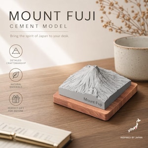 Könnte beinhalten: Ein Zementmodell des Mount Fuji, das auf einem Holzsockel steht. Das graue Bergmodell weist eine detaillierte Verarbeitung auf und trägt den Text "Mount Fuji". Das Bild enthält auch den Text "Bringen Sie den Geist Japans auf Ihren Schreibtisch."