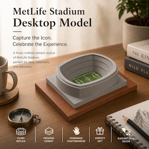 May include: A gray cement replica of MetLife Stadium, featuring a green field, sits on a wooden base. The model is a desktop decor item. The text reads "MetLife Stadium Desktop Model". A compass and books are also visible.