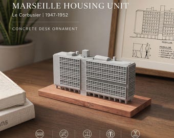 Op de afbeelding: Een grijs betonnen bureauornament dat de Marseille Housing Unit van Le Corbusier voorstelt, met een gedetailleerde rastergevel en een plat dak. Het architecturale model is gemonteerd op een rechthoekige houten voet met een natuurlijke nerf.
